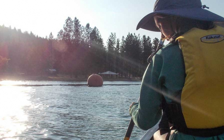 a girl wearing a yellow life jacket paddles a canoe